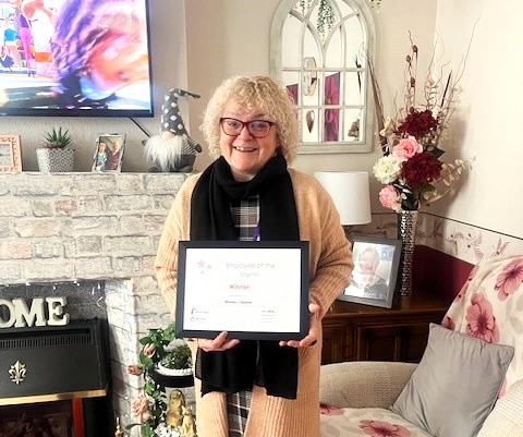 Maxine proudly displays her certificate to the camera with a big smile.