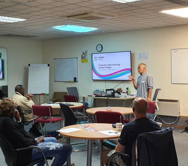 Trainer Dave stands at the front of a room delivering training.