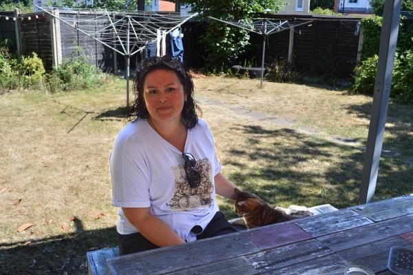 Kirsty sits in the garden stroking a cat in the sunshine.