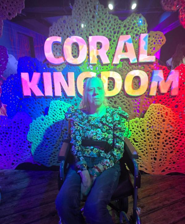 Linda sits in front of a sign saying Coral Kingdom.