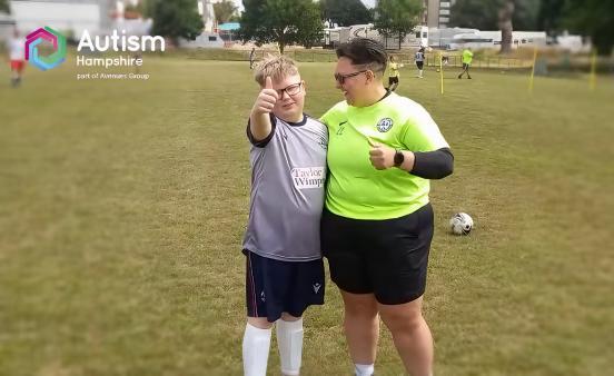 Lucie and one of her football players stand on the pitch giving a thumbs up.