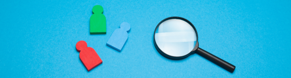 Wooden people shaped pieces and a magnifying glass on a blue background