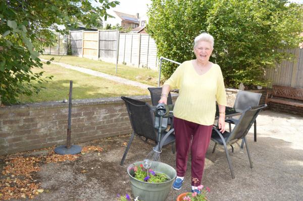 One of the ladies we support smiling in her garden watering her flower pots.