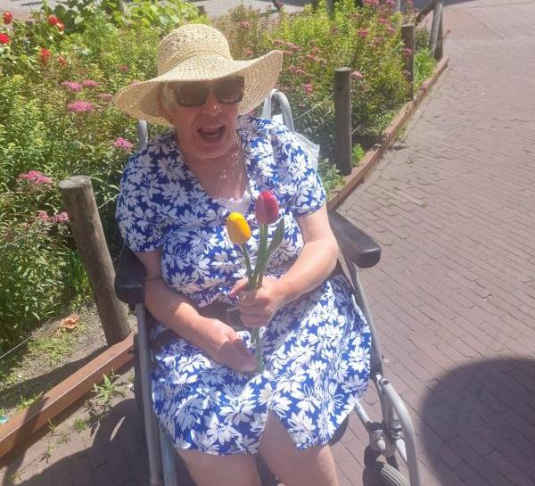 A woman in blue sitting in her wheelchair, proudly holding two wooden tulips in Amsterdam.