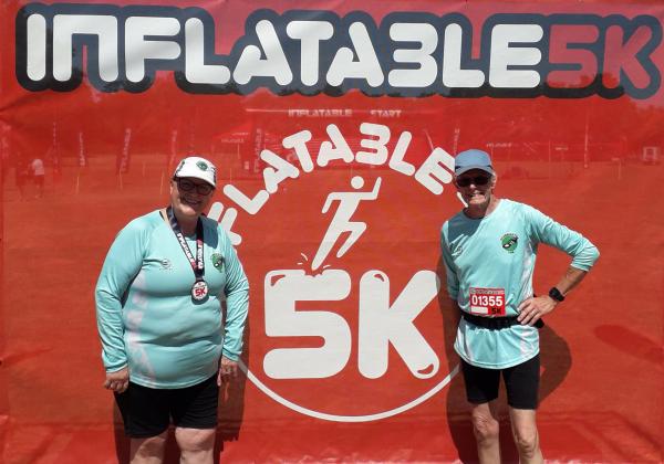 Sue and her husband stand in front of the Inflatable 5k banner