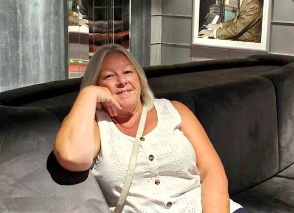 Mandy smiles at the camera sitting on a grey sofa.