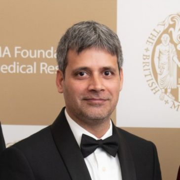 A person in a dinner jacket and bow tie (Zia Katshu) is smiling at the camera