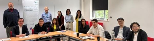 12 people sitting around desks and smiling at the camera