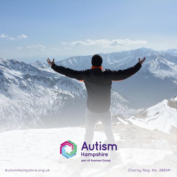 A man stands on the top of mountains with his arms open wide.