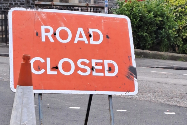 oad closed sign on a street, with a traffic cone in the foreground.